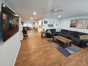 Ein geräumiges Wohnzimmer mit einem großen schwarzen Ecksofa, einem Holztisch und einem Essbereich mit Tisch und Stühlen.