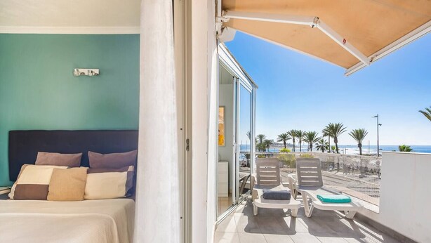Una camera da letto con un letto, vista sulla spiaggia e un balcone con sedie e un tavolo.