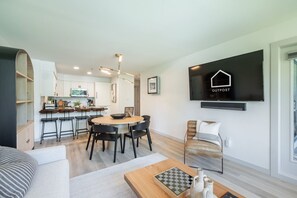 Uma sala de estar moderna com área de jantar, cozinha ao fundo e uma televisão de tela plana montada exibindo 'OUTPOST'.