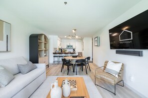 A modern living room with a sofa, a coffee table with vases, a dining area with a table and chairs, and a kitchen in the background. - Ski-in/out | Complex pool, hot tub & BBQ | WIFI (Whistler)