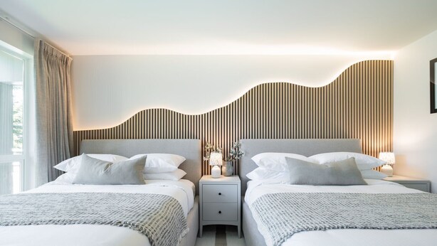 A modern hotel room with two beds, a nightstand with a lamp, and a wall with vertical wooden slats. - Ski-in/out | Complex pool, hot tub & BBQ | WIFI (Whistler)