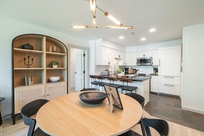 Uma cozinha moderna com armários brancos, uma ilha central e um espaço de refeições com mesa redonda e cadeiras.