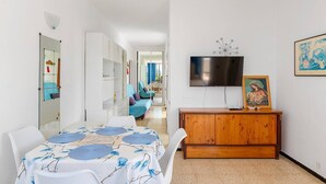 A modern living room with a dining table, a TV, and a wooden cabinet. - 2 Bedroom Apartment with Seaview (Costa Adeje-Playas De Fañabe)
