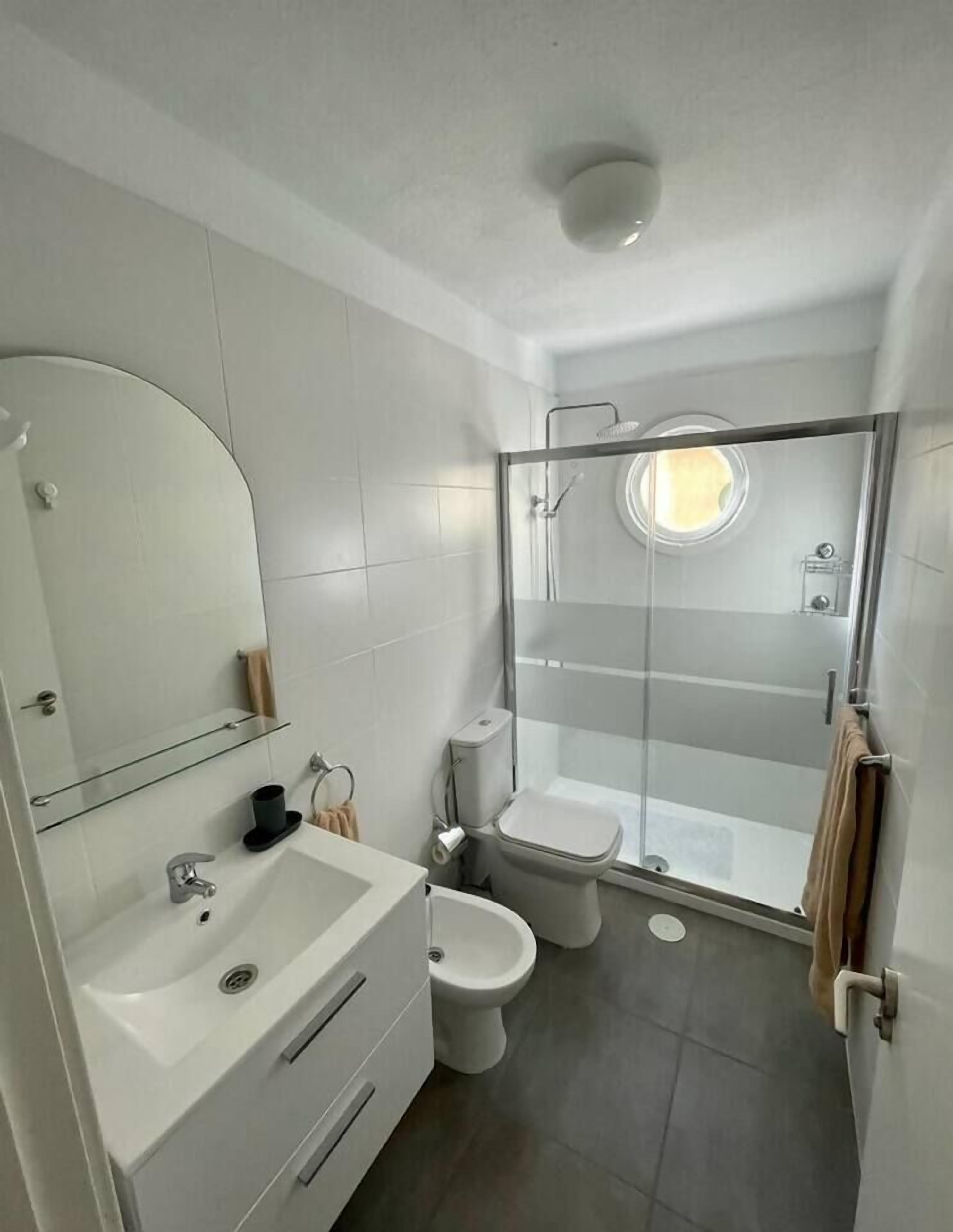 Un baño moderno con ducha de vidrio, lavamanos, inodoro y espejo.