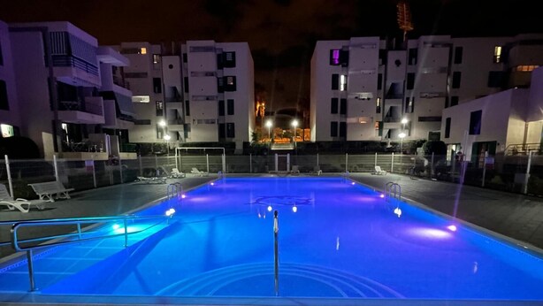 Une piscine d’une profondeur de 0,80 mètre, entourée d’une clôture, avec des chaises longues et une vue sur les bâtiments adjacents.
