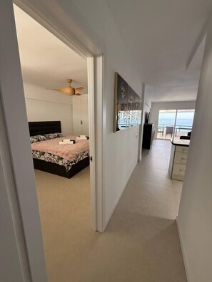 Ein Korridor führt zu einem Schlafzimmer mit einem Bett, einem Deckenventilator und Blick aufs Meer.