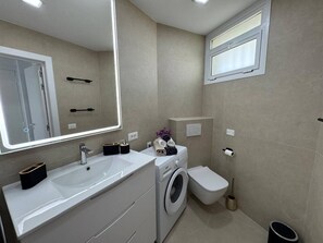 Ein modernes Badezimmer mit Waschbecken, Spiegel, Waschmaschine, Toilette und einem Fenster.