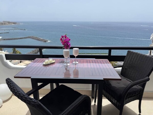 Ein Balkon mit Tisch, zwei Stühlen, einer Blumenvase und Blick aufs Meer.