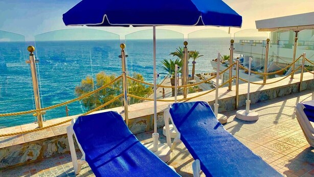 Zwembadgedeelte met ligbedden en een blauwe parasol, met uitzicht op zee.