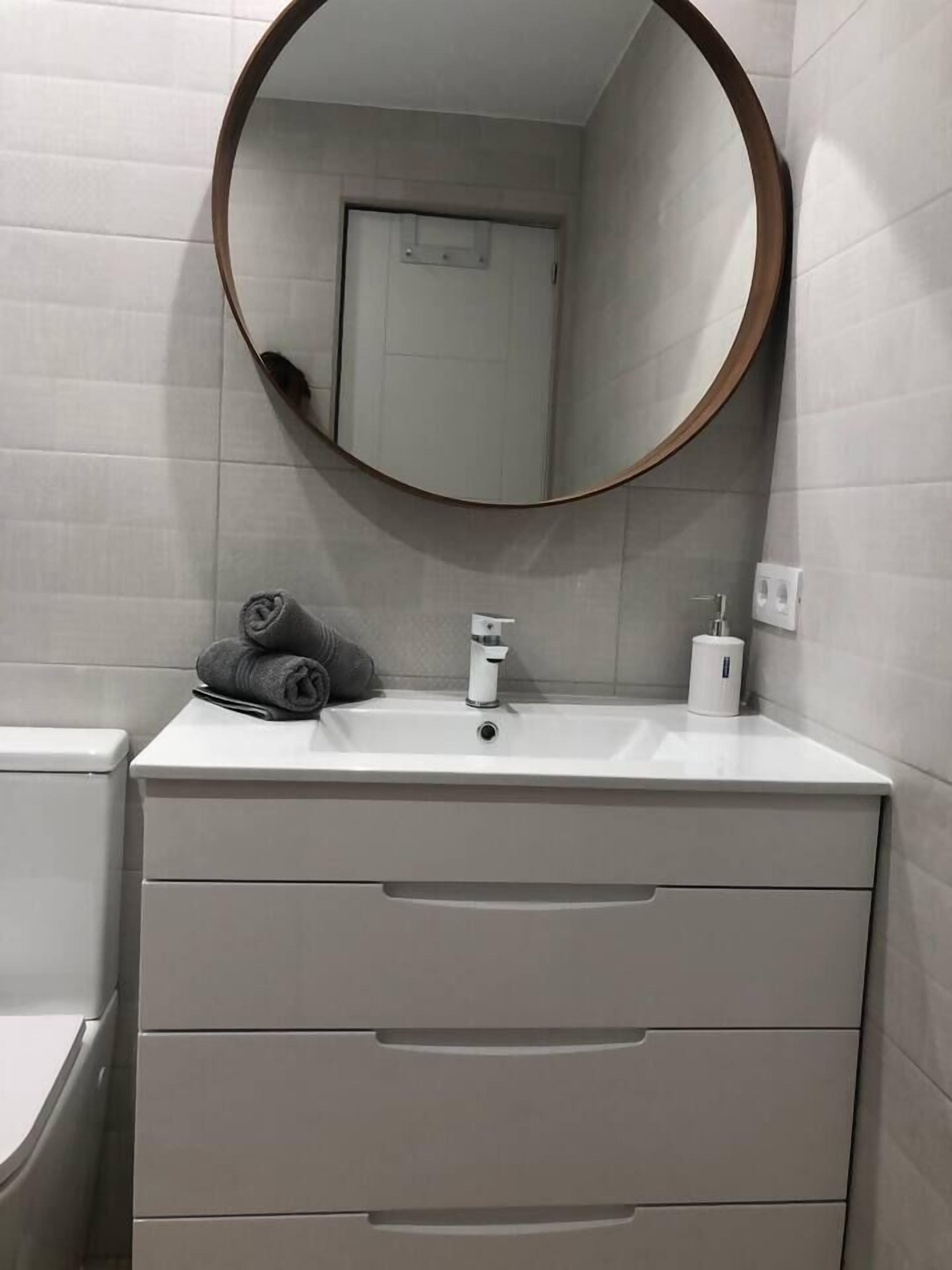 A bathroom with a round mirror, a white sink, a towel, and a toilet.