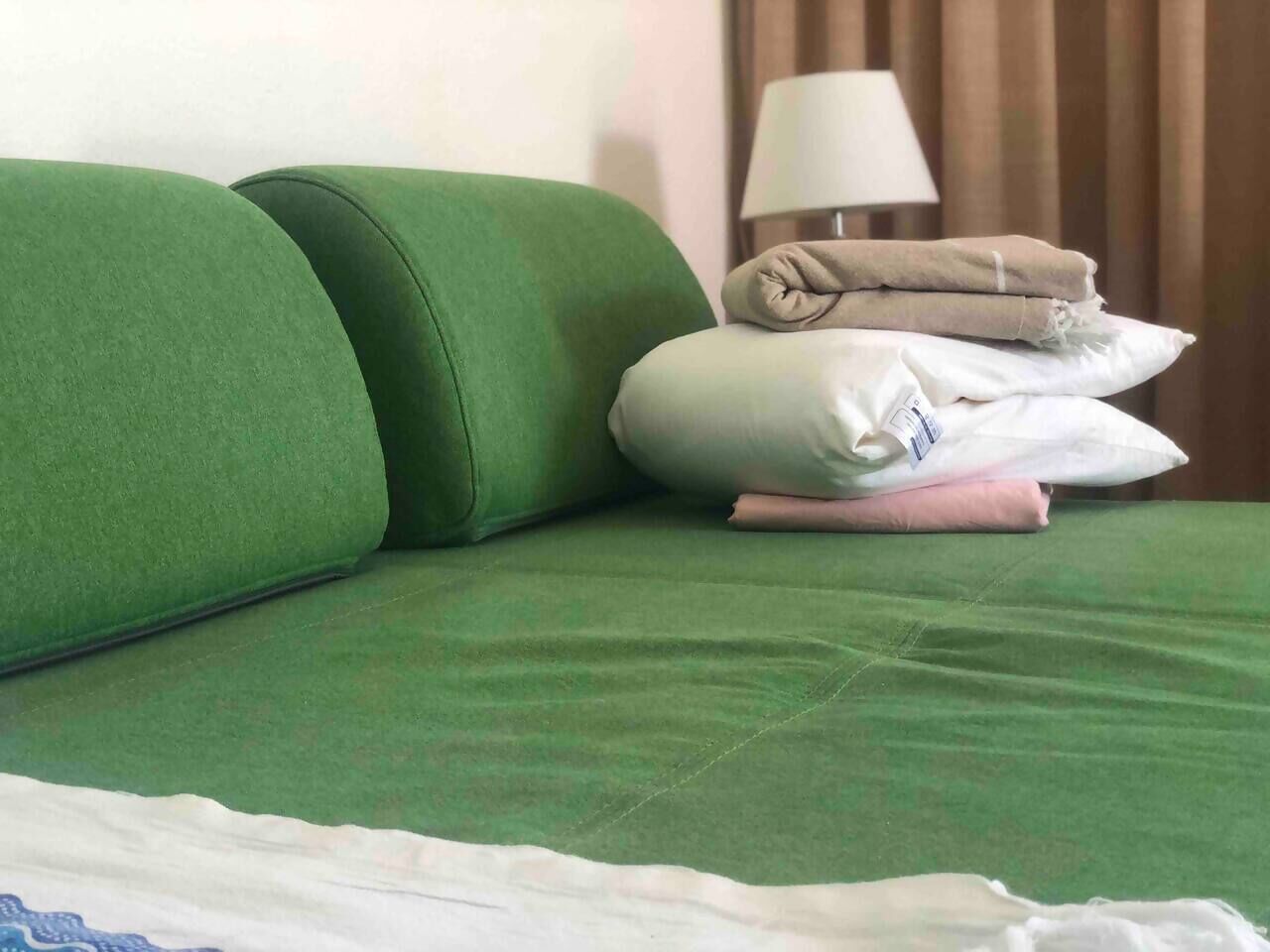 Un lit avec une literie verte, des oreillers et une couverture pliée.