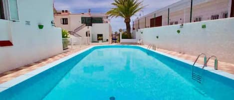 A rectangular swimming pool with a clear blue water surface, surrounded by white walls and a tiled floor.