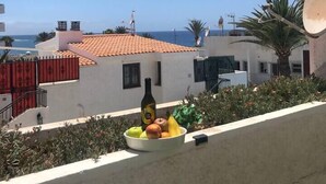 A balcony with a bottle, fruits, and a view of the sea and buildings. - Playa Troya Apartment at the beach (Costa Adeje)