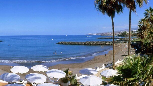 A beach with umbrellas, palm trees, and a clear blue sky. - Playa Troya Apartment at the beach (Costa Adeje)