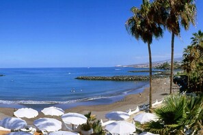 Ein Strand mit Sonnenschirmen, Palmen und einem strahlend blauen Himmel.