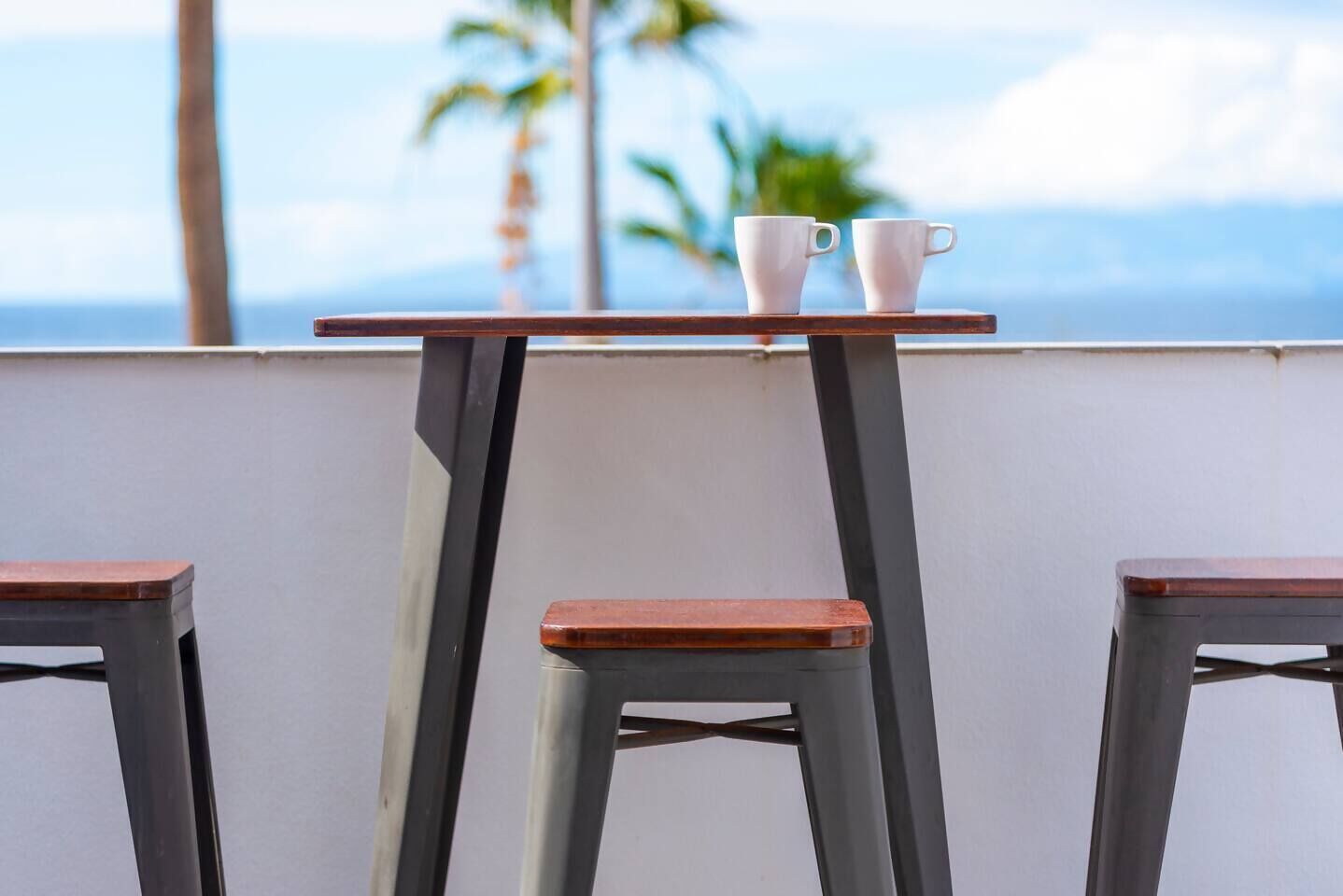 Una mesa con dos tazas blancas y vista al océano y palmeras.