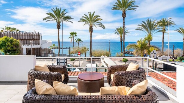 Una terrazza sul tetto con mobili in vimini, un tavolo rotondo e vista sul mare e sulle palme.