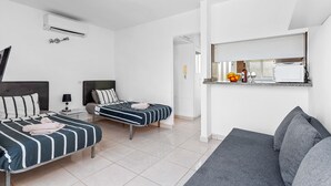 A hotel room with two beds, a sofa, a small table, a mirror, and an air conditioning unit. - Beachfront Studio Las Americas (Costa Adeje)