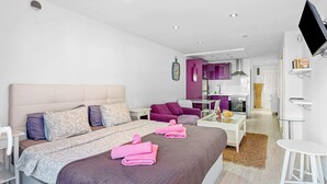 Moderni hotellihuone, jossa on suuri sänky, työpöytä, tuoli, televisio ja pieni keittiönurkkaus.