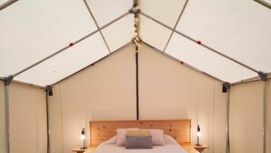 A tented room with a bed, bedside lamps, a wooden chest, and a patterned rug. - Sorrel Tent | Canvas Tent with Lake Access (Kirkfield)