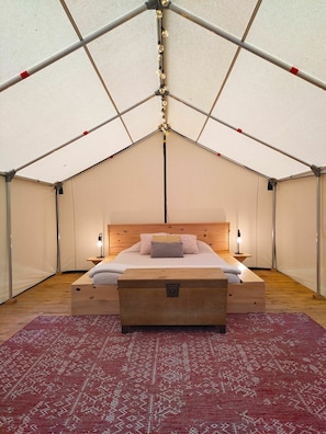 Una tenda con un letto, abat-jour, un baule di legno e un tappeto decorato.