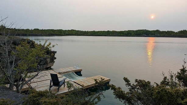 A wooden dock extending into calm water, surrounded by trees and vegetation. - Sorrel Tent | Canvas Tent with Lake Access (Kirkfield)