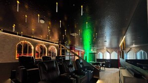 Een kamer met een donker plafond, groen licht en een zithoek met lederen stoelen.