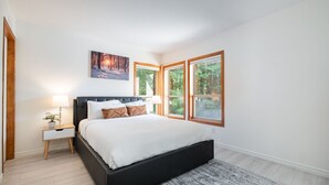 A bedroom with a large bed, a nightstand with a lamp, and a painting above the bed. - Excellent Ski-in/out | Complex hot tub | BBQ (Whistler)