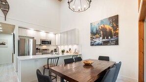 A modern kitchen with white cabinets, stainless steel appliances, and a wooden dining table with chairs. - Excellent Ski-in/out | Complex hot tub | BBQ (Whistler)