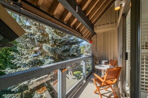 A balcony with a wooden ceiling, a table with chairs, and a view of snow-covered trees. - Townhome Near Blackcomb Lift | BBQ | Free Parking (Whistler)