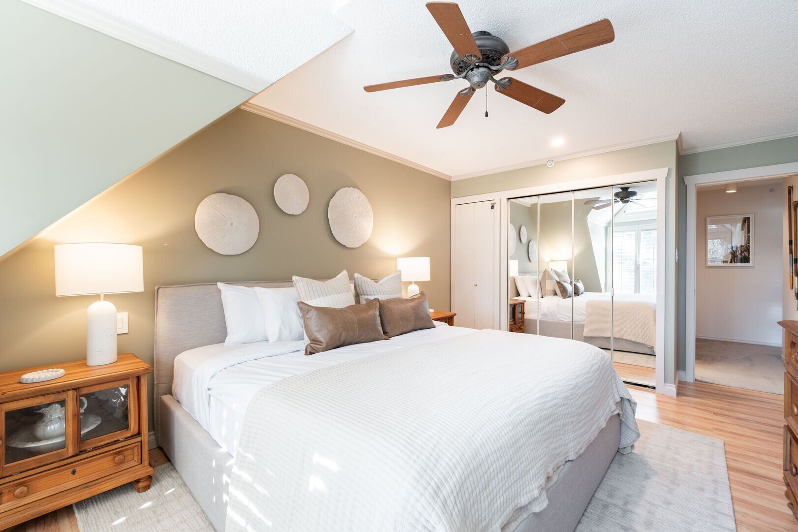 A bedroom with a large bed, ceiling fan, bedside lamps, and a wooden cabinet.