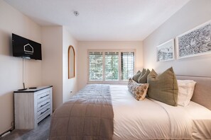 A bedroom with a bed, a TV, a dresser, a window with blinds, and framed artwork on the wall. - Townhome Near Blackcomb Lift | BBQ | Free Parking (Whistler)