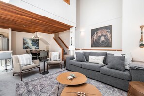A modern living room with a grey sofa, a coffee table, and a painting of a bear on the wall. - Townhome Near Blackcomb Lift | BBQ | Free Parking (Whistler)