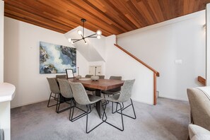 A dining area with a wooden table and six chairs, a modern chandelier, and a painting on the wall. - Townhome Near Blackcomb Lift | BBQ | Free Parking (Whistler)