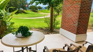 Een terras met een ronde tafel en stoelen, een bakstenen pilaar en uitzicht op een golfbaan.