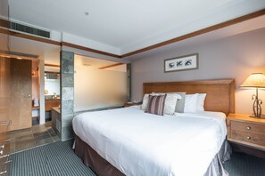 A hotel room with a large bed, wooden headboard, a nightstand, a lamp, and a bathroom visible through an open door. - Blackcomb Ski-in/out | Complex pool & hot tub (Whistler)