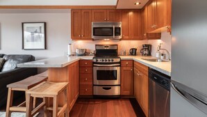 A compact kitchen with wooden cabinets, stainless steel appliances, and a built-in oven. - Blackcomb Ski-in/out | Complex pool & hot tub (Whistler)
