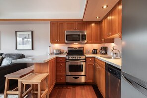 A compact kitchen with wooden cabinets, stainless steel appliances, and a built-in oven. - Blackcomb Ski-in/out | Complex pool & hot tub (Whistler)