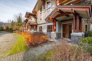 A two-story house with a stone foundation, large windows, and a covered porch. - Private Hot Tub | Central AC | BBQ | Garage (Whistler)