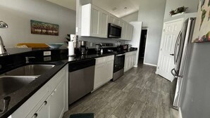Una cocina moderna con armarios blancos, electrodomésticos de acero inoxidable y piso de baldosas grises.