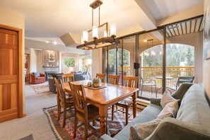 A spacious living area with a wooden dining table, a sofa, and a balcony with a railing. - Penthouse, Mountain Views, Ski-In/Out, Pool, Hot Tub, Gym (Whistler)