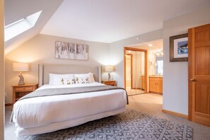 Une chambre avec un grand lit, deux tables de chevet avec des lampes, une lucarne au plafond et une vue sur la salle de bain.