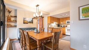 Un comedor con una mesa y sillas de madera, un candelabro y vista a la cocina al fondo.