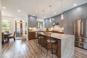A modern kitchen with grey cabinets, a stainless steel refrigerator, and a marble island with bar stools. - Luxury | Private garage | Private hot tub | BBQ (Whistler)