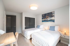 Ein Hotelzimmer mit zwei Betten, einem Schreibtisch, einem Sessel, einem Nachttisch und einem Gemälde an der Wand.