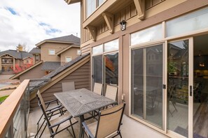 A residential building with a balcony featuring a table and chairs, large windows, and a staircase leading to the upper floor. - Luxury | Private garage | Private hot tub | BBQ (Whistler)