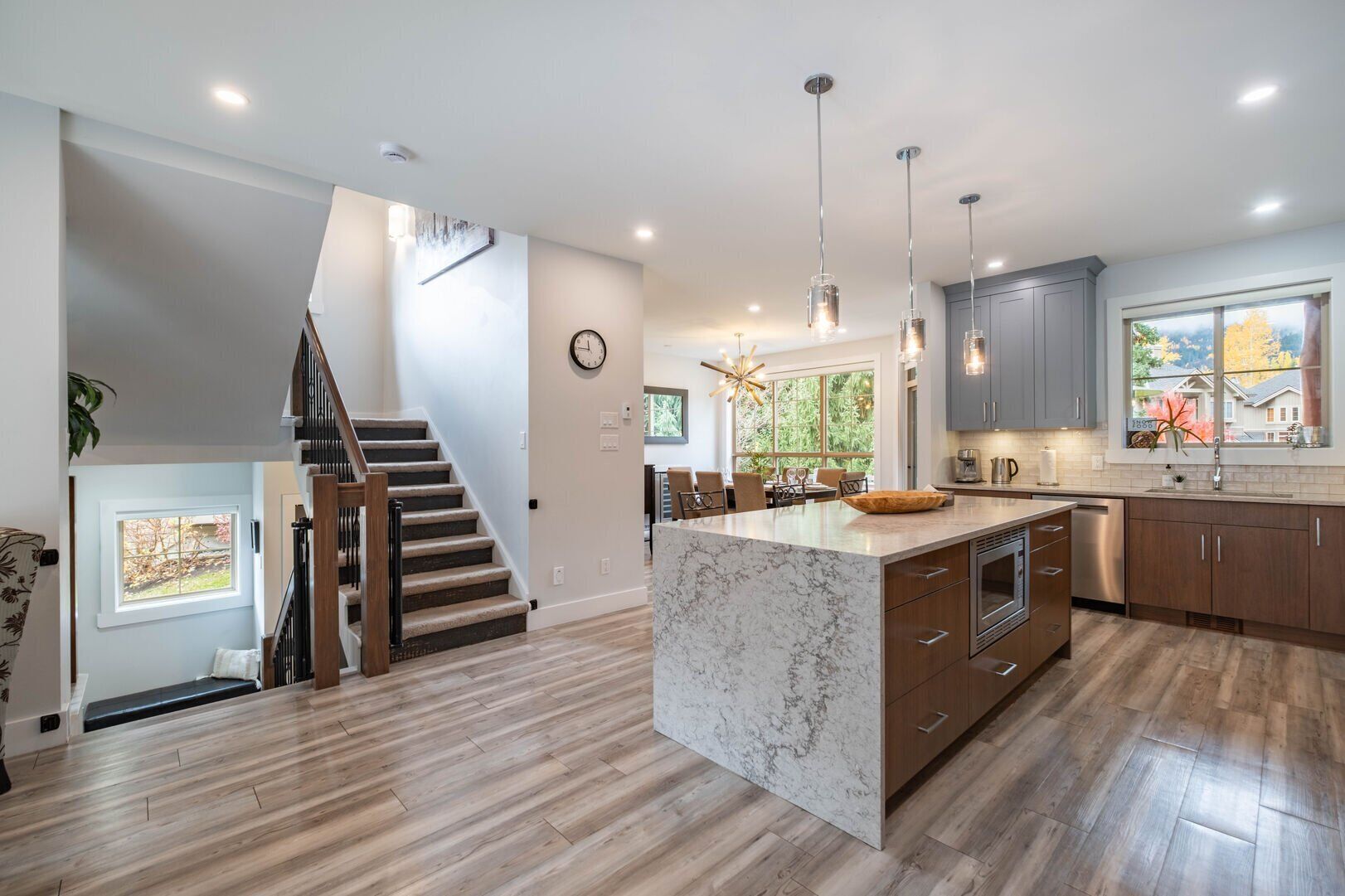 A modern kitchen with a large island, wooden flooring, and a staircase leading to an upper level.
