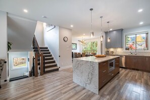 A modern kitchen with a large island, wooden flooring, and a staircase leading to an upper level. - Luxury | Private garage | Private hot tub | BBQ (Whistler)