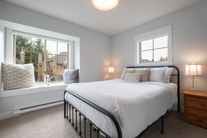 A bedroom with a bed, two bedside tables, and two windows. - Luxury | Private garage | Private hot tub | BBQ (Whistler)