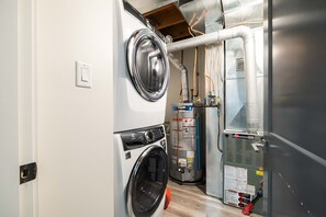A compact laundry room with a front-loading washer and dryer, a water heater, and a ventilation unit. - Luxury | Private garage | Private hot tub | BBQ (Whistler)